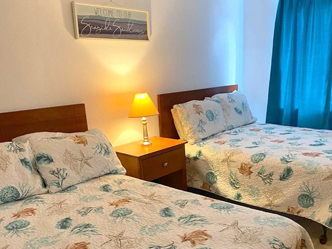 A bedroom with two beds, a nightstand, and a lamp