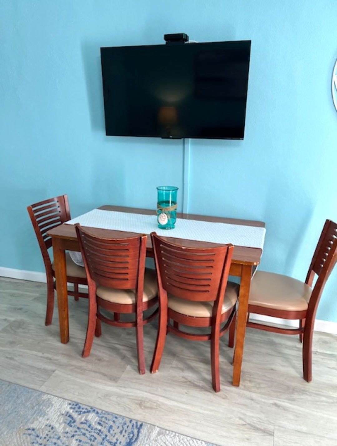 A dining room with a table and chairs and a flat screen tv on the wall.