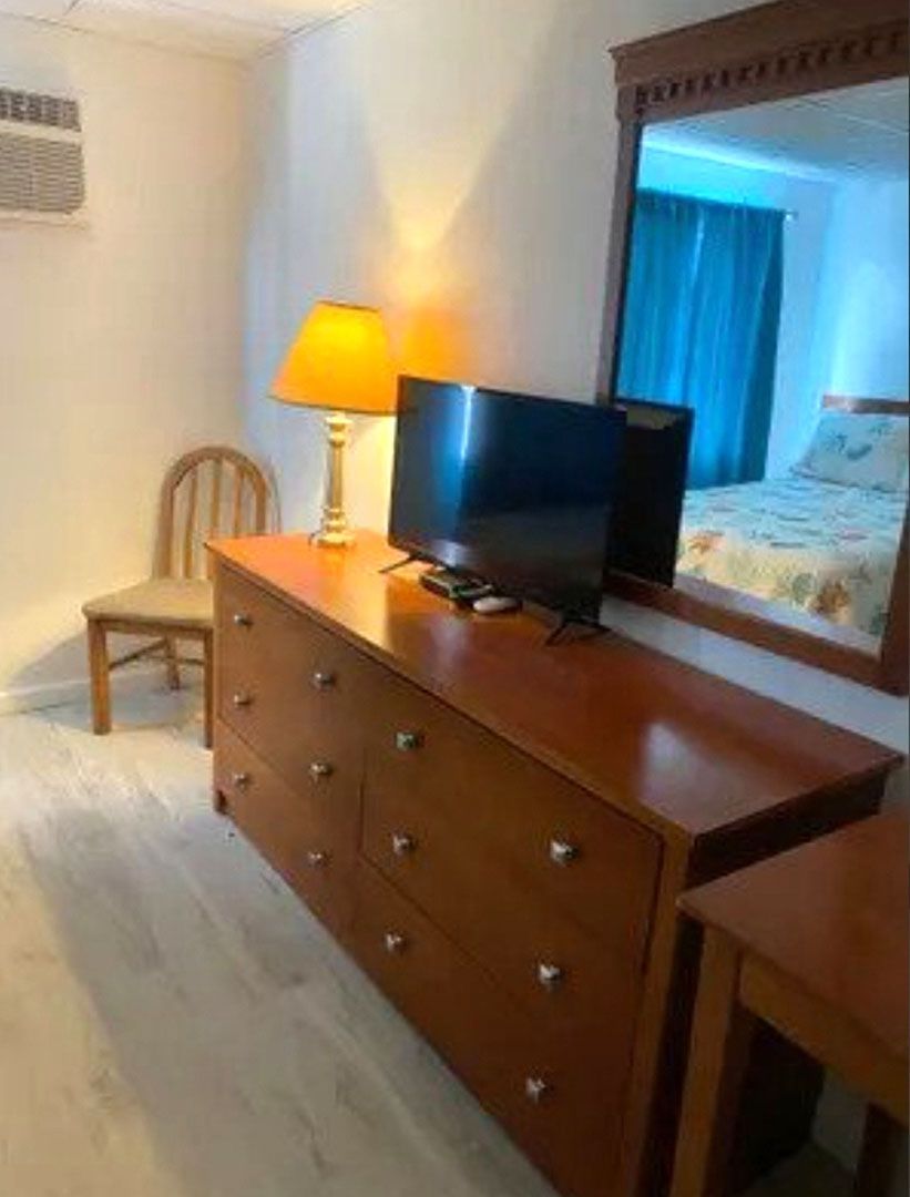A bedroom with a dresser, television, lamp, chair, and mirror.