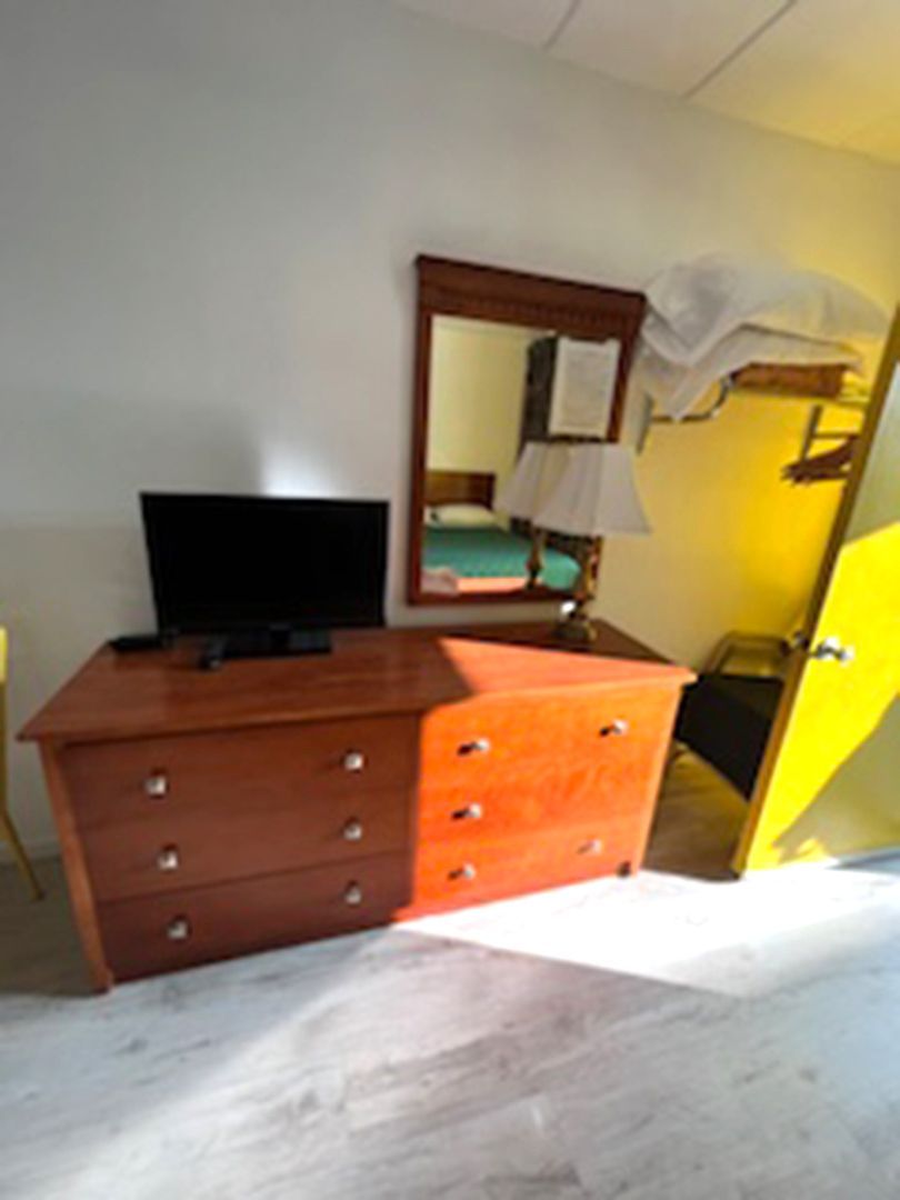 A bedroom with a dresser a television and a mirror
