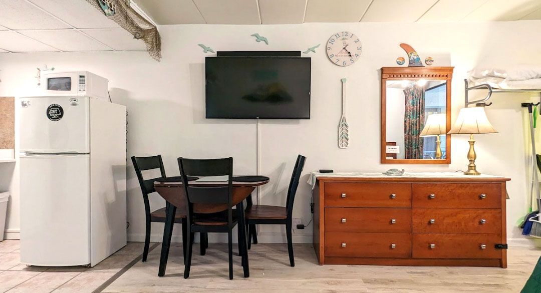 A living room with a table, chairs, dresser, refrigerator, and television.