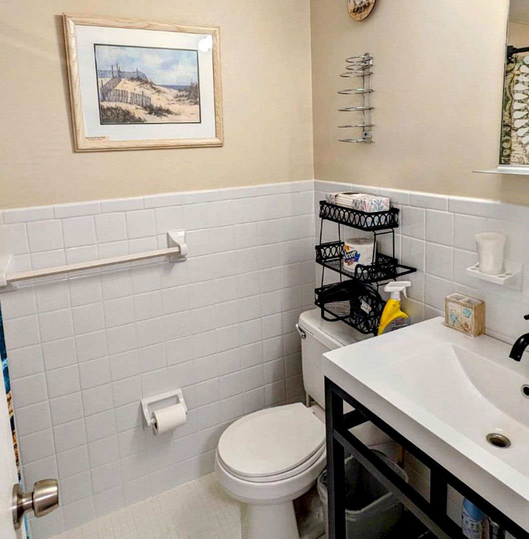 A bathroom with a toilet, sink, and picture on the wall.