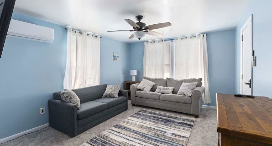 A living room with a couch, rug, television, and ceiling fan.