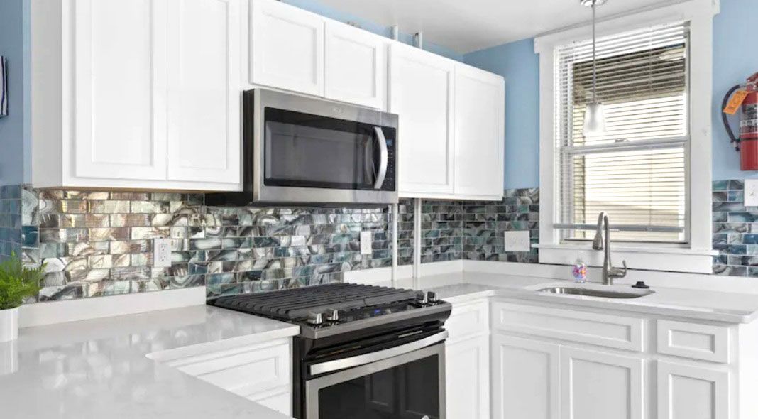 A kitchen with white cabinets, stainless steel appliances, a stove, microwave, sink, and window.
