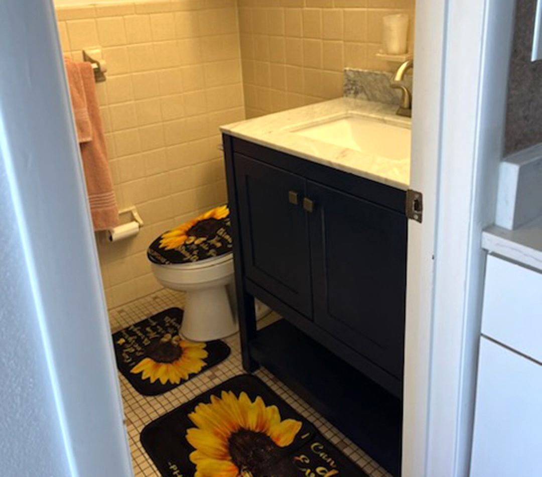 A bathroom with a toilet a sink and a rug with sunflowers on it