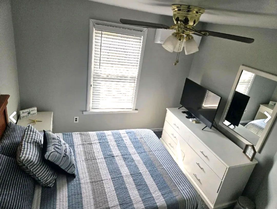 A bedroom with a bed, dresser, television, and ceiling fan.