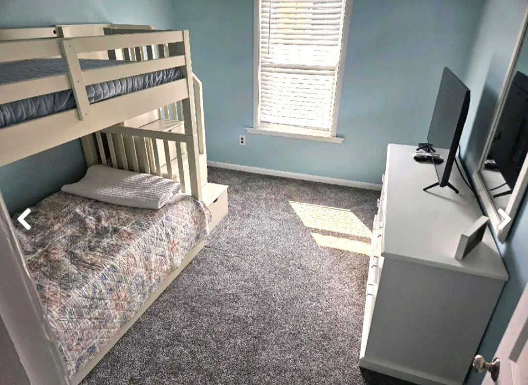 A bedroom with a bunk bed, dresser, and television.