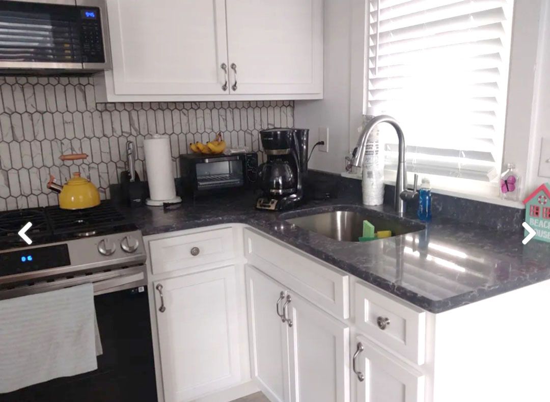 A kitchen with white cabinets, a sink, stove, and microwave.