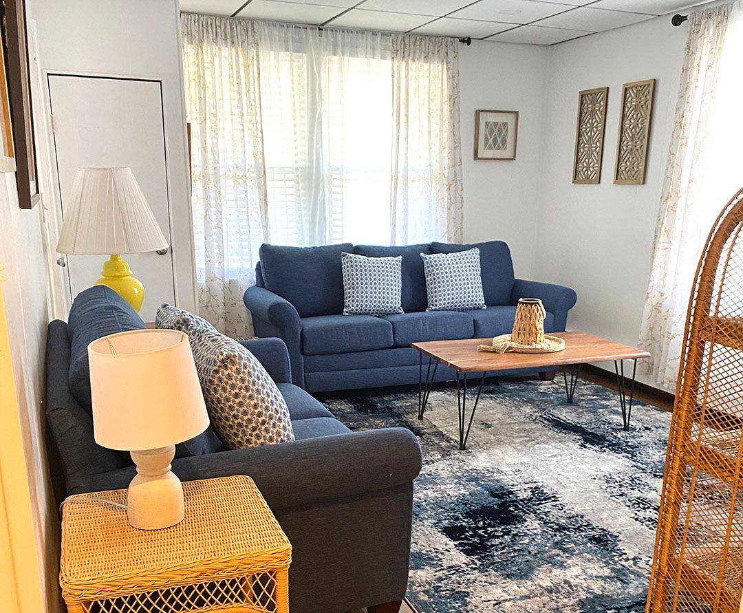 A living room with a blue couch, wicker chair, coffee table, and lamp.