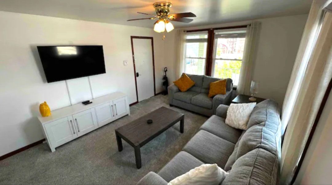 A living room with a couch, table, television, and ceiling fan.