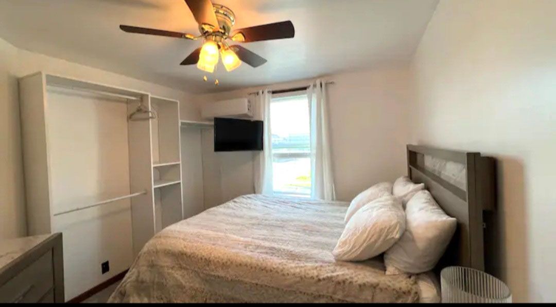 A bedroom with a bed, ceiling fan, and television.