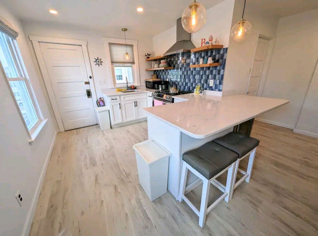 A kitchen with a large island, stools, and a trash can.