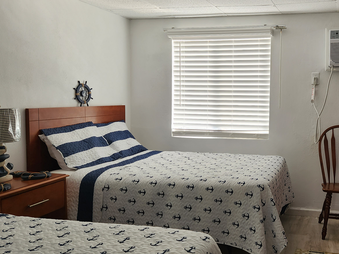 Bedroom with two twin beds, blue and white nautical bedding, a wooden headboard, and blinds.