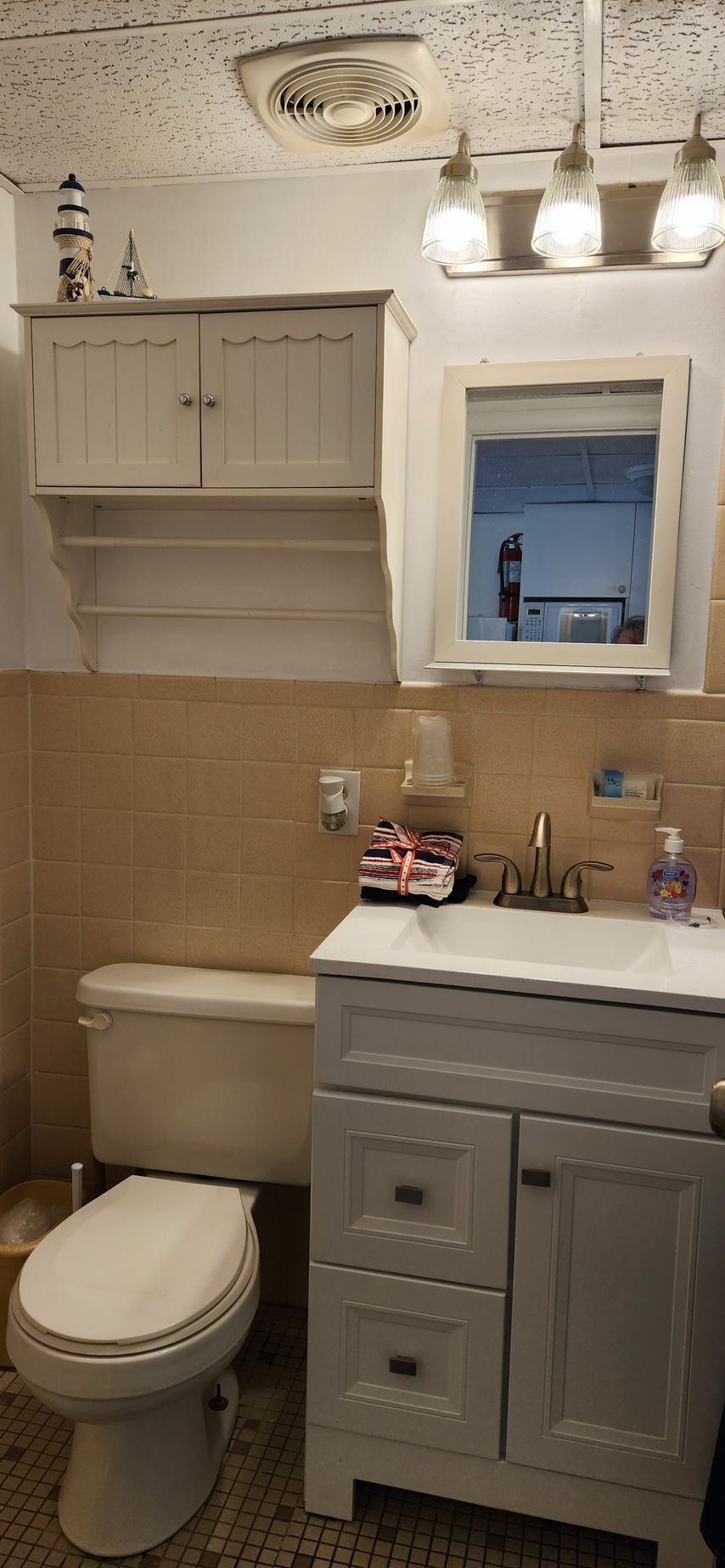 Bathroom with gray vanity, toilet, and wall-mounted storage cabinet. Beige tile walls, white ceiling.