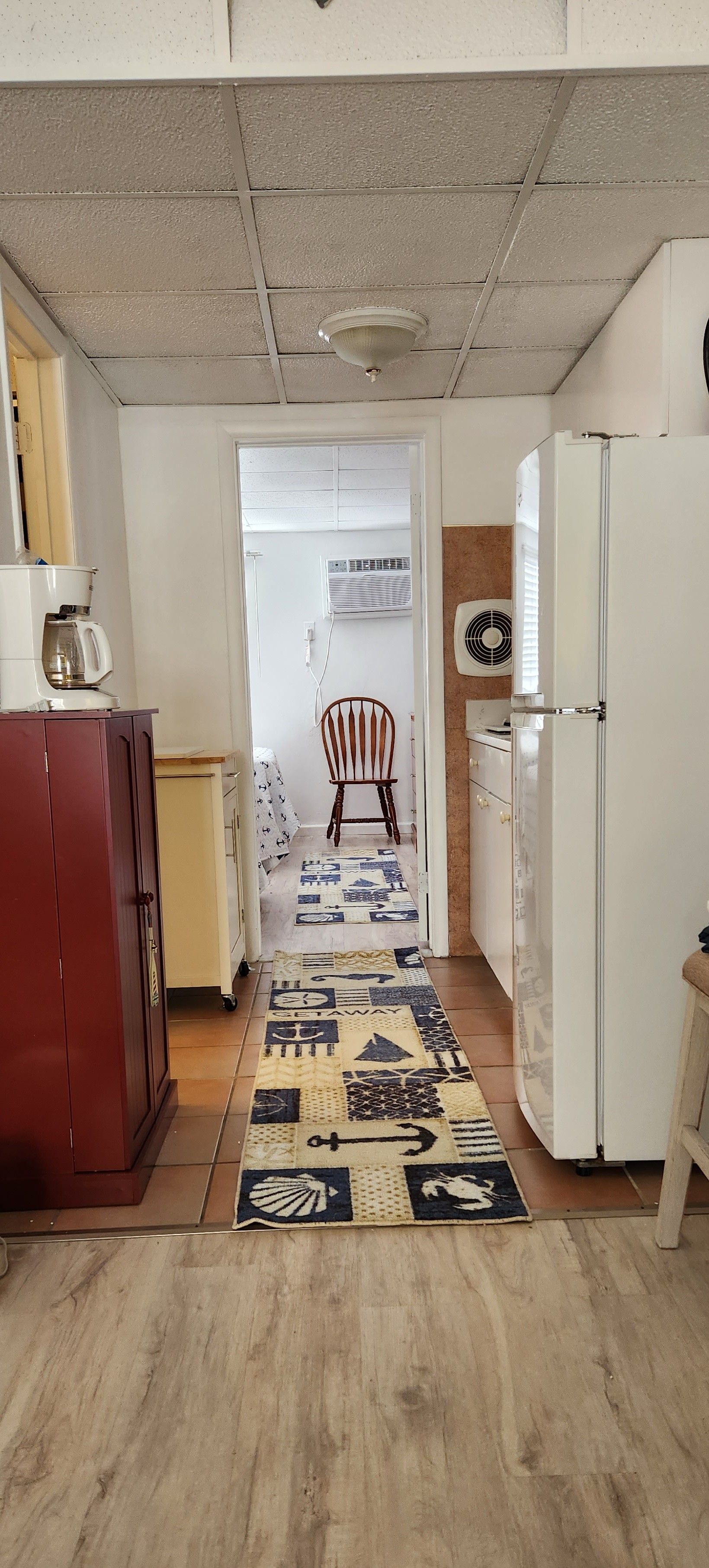 Kitchen interior with red cabinet, white refrigerator, patterned rug, and doorway leading to another room.