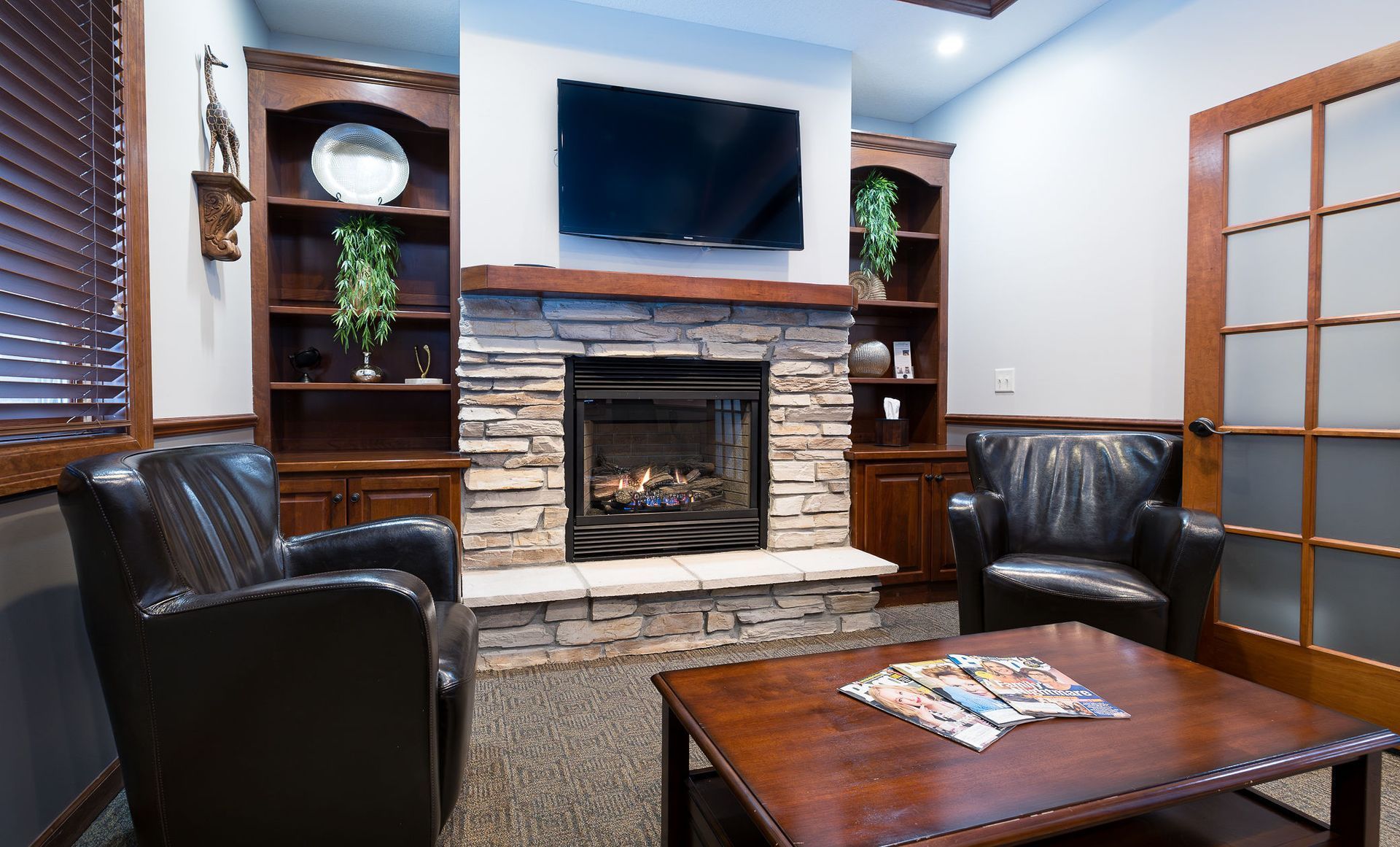Cozy waiting room with fireplace, bookshelves, leather chairs, and a coffee table with magazines.