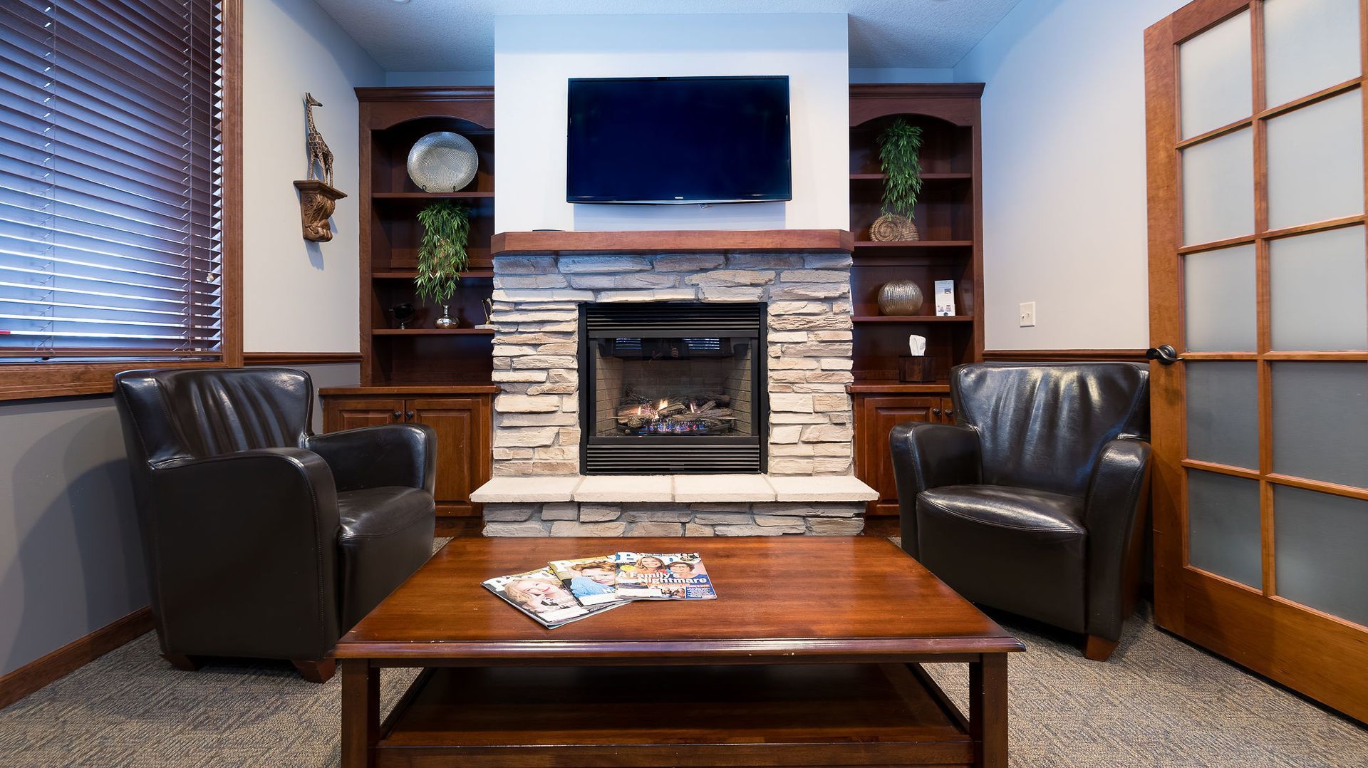 Cozy room with fireplace, built-in shelves, two leather armchairs, coffee table, and frosted glass door.