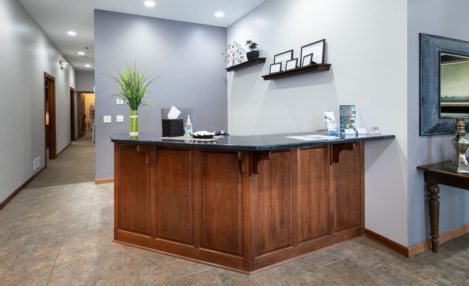 Reception desk in a clinic hallway. Wooden desk with a dark countertop, gray walls, and flower arrangement.