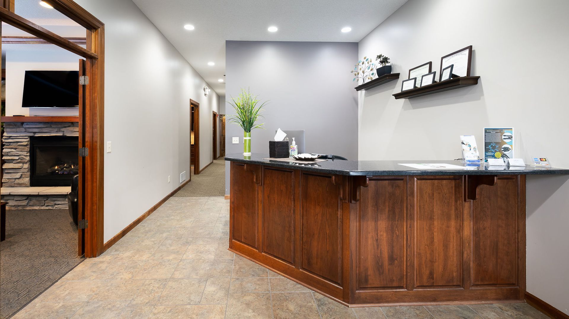 Reception area with dark wood desk, gray walls, and hallway leading to doors.
