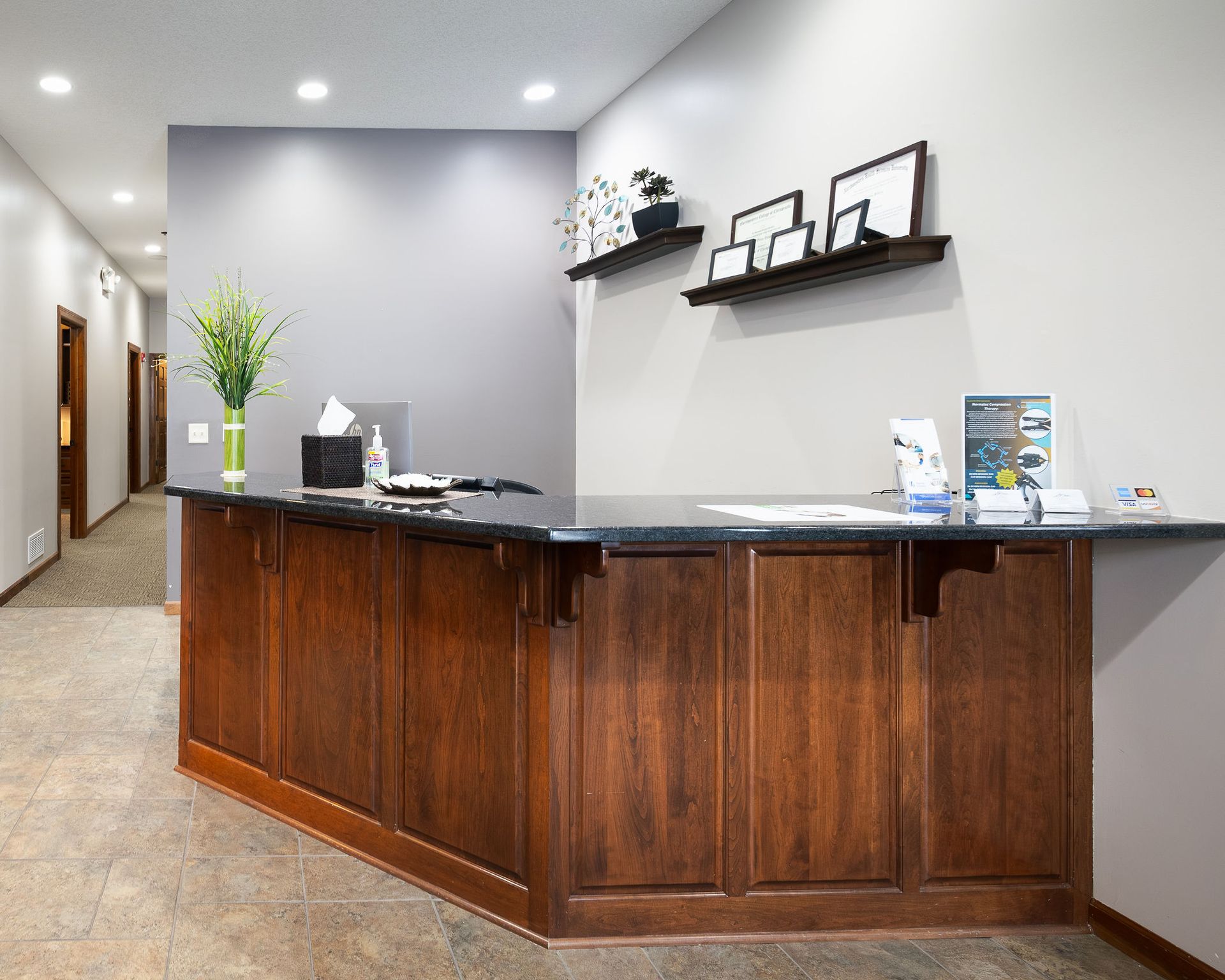 Reception desk in a clinic hallway. Dark wood cabinetry, gray countertops, and light gray walls.