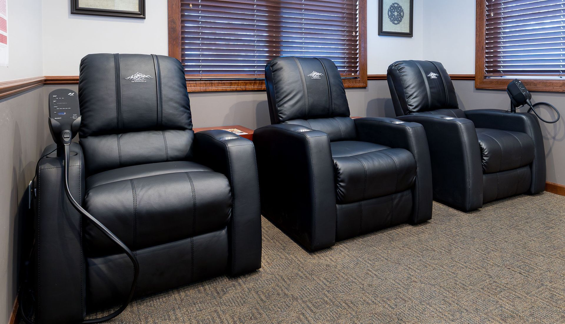 Three black recliners in a room with brown blinds and carpet.