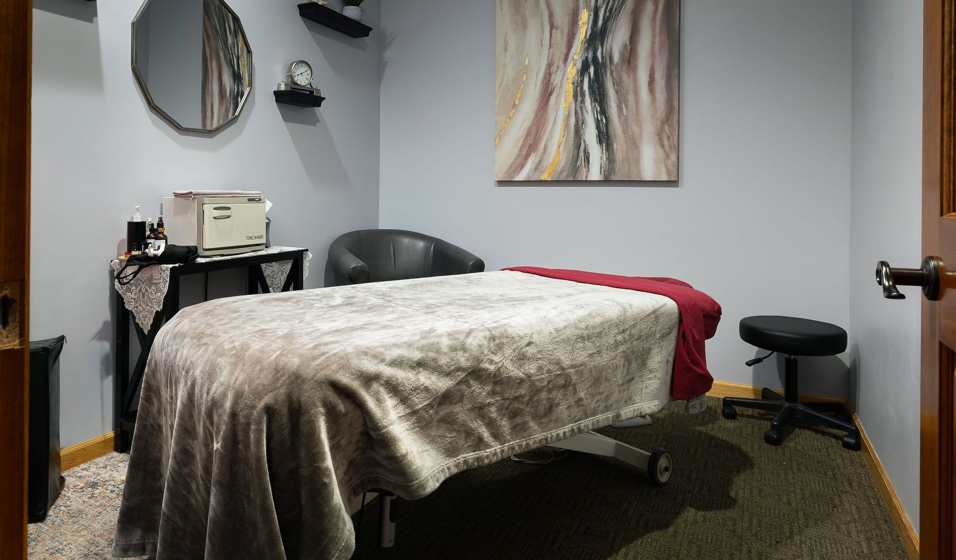 Massage room with a massage table, chair, artwork, and equipment.