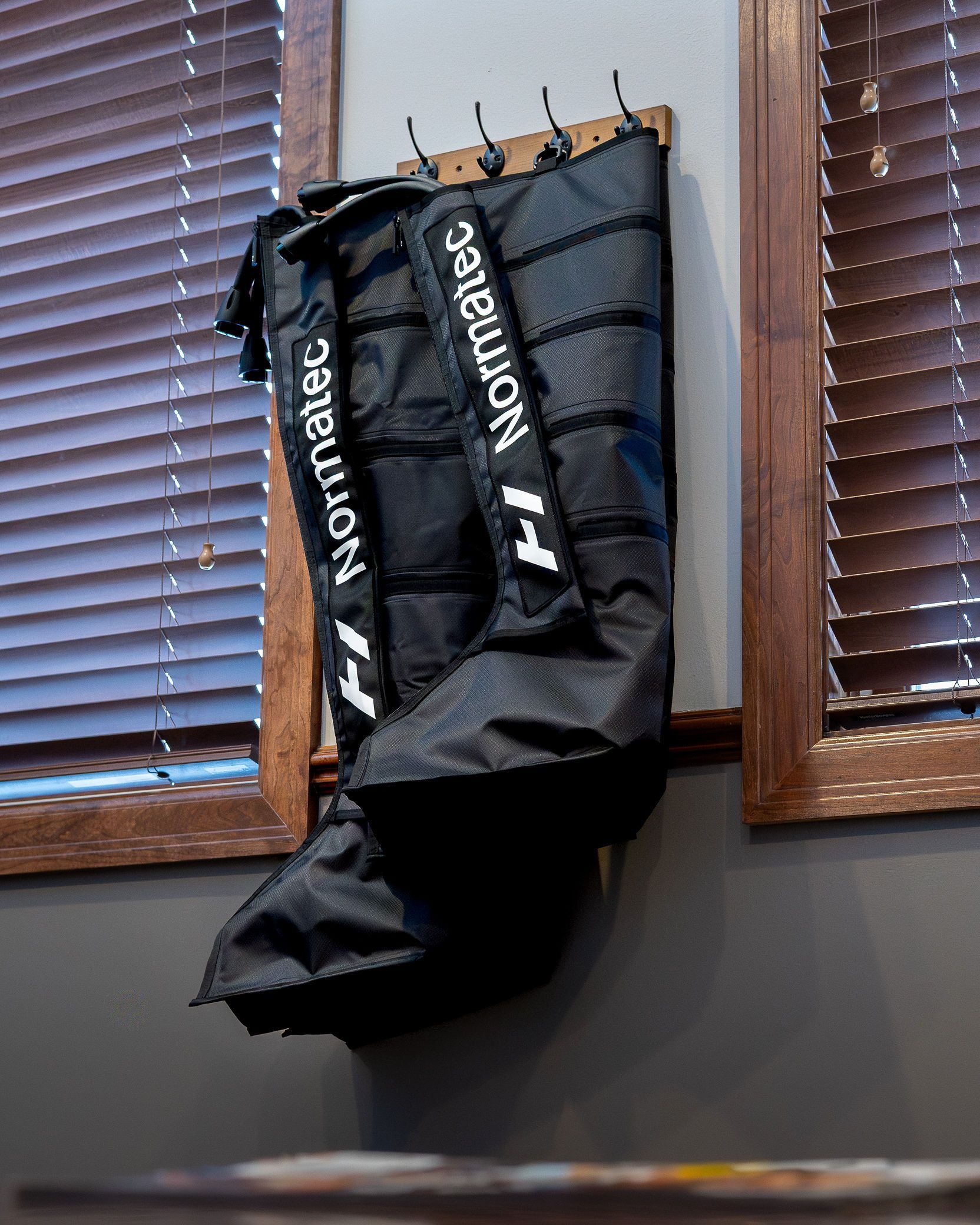 Black Normatec compression boots hanging on a wooden board against a window.
