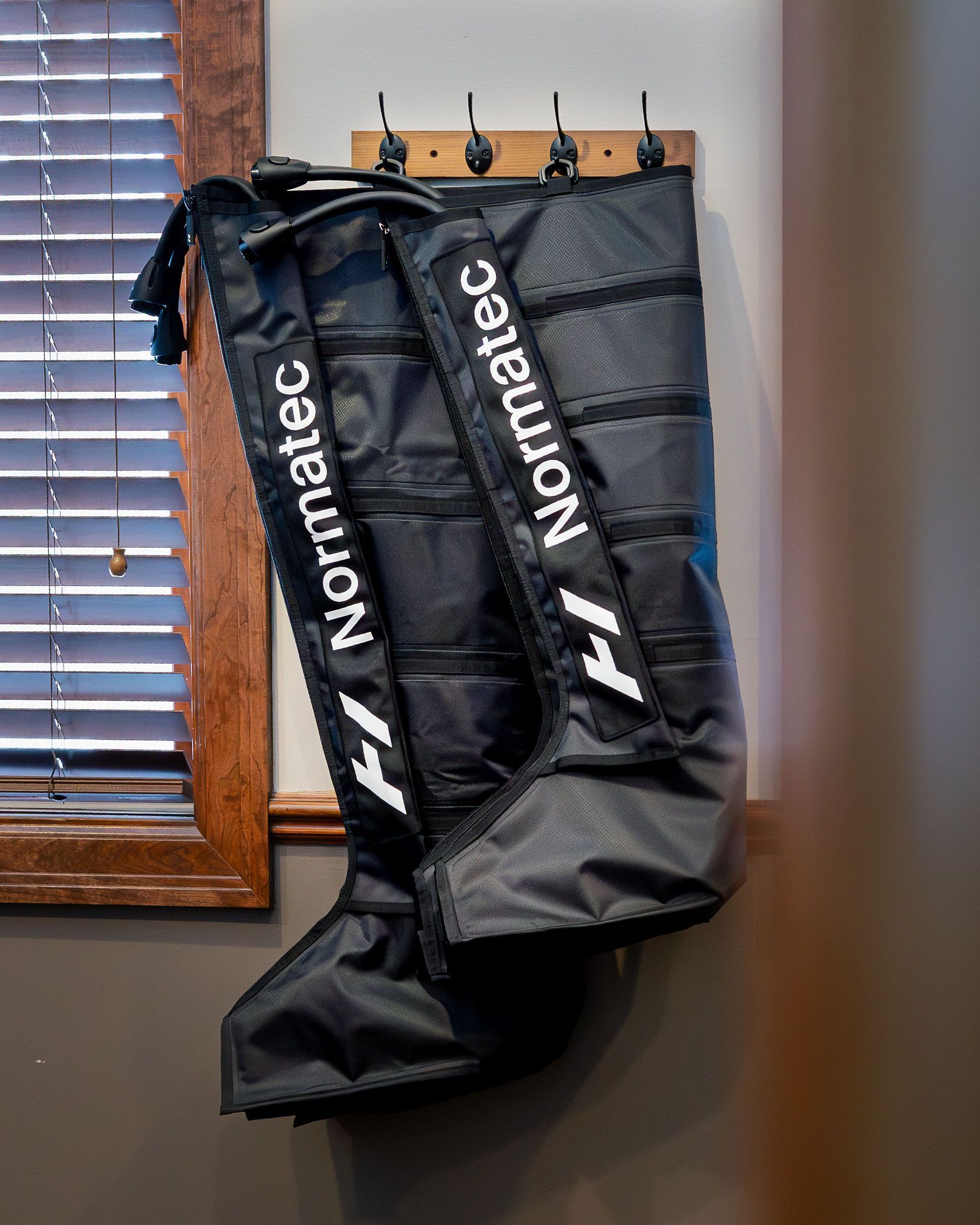 Black Normatec recovery boots hanging on a wooden wall.