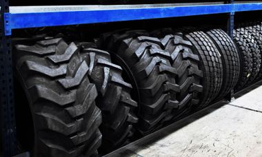 A row of tires are lined up on a shelf in a warehouse.