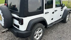 A white jeep with a black top is parked on gravel.