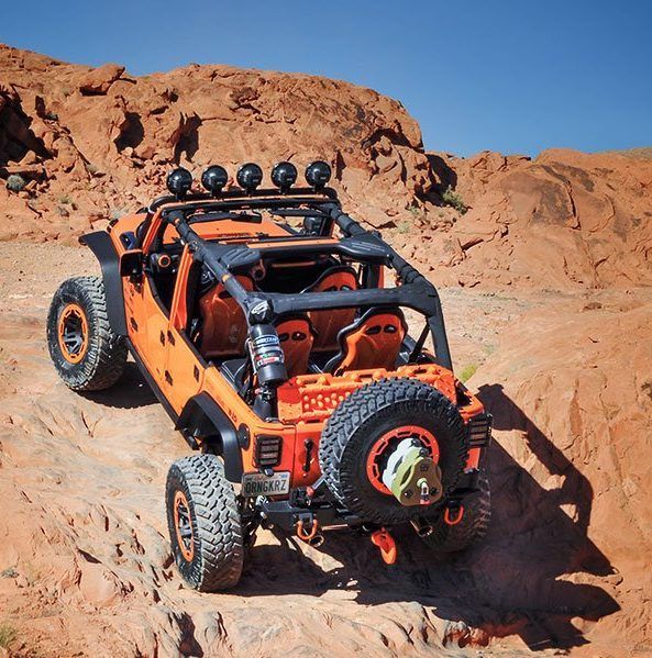 An orange jeep is parked on a dirt road