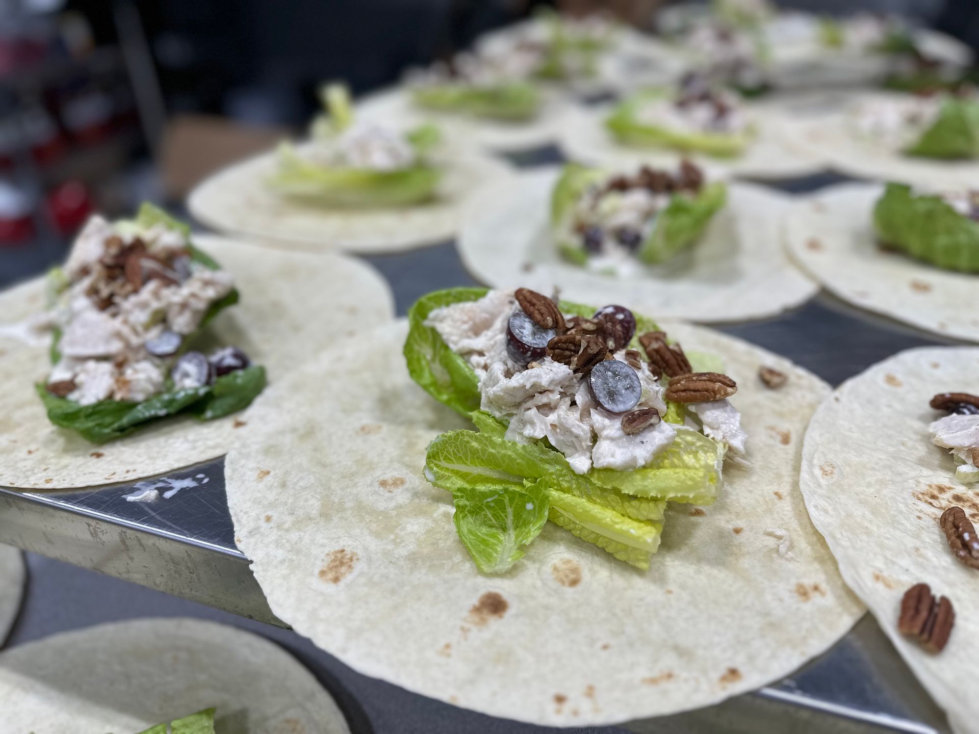Tortillas topped with lettuce, chicken salad, and pecans arranged on a metal surface.