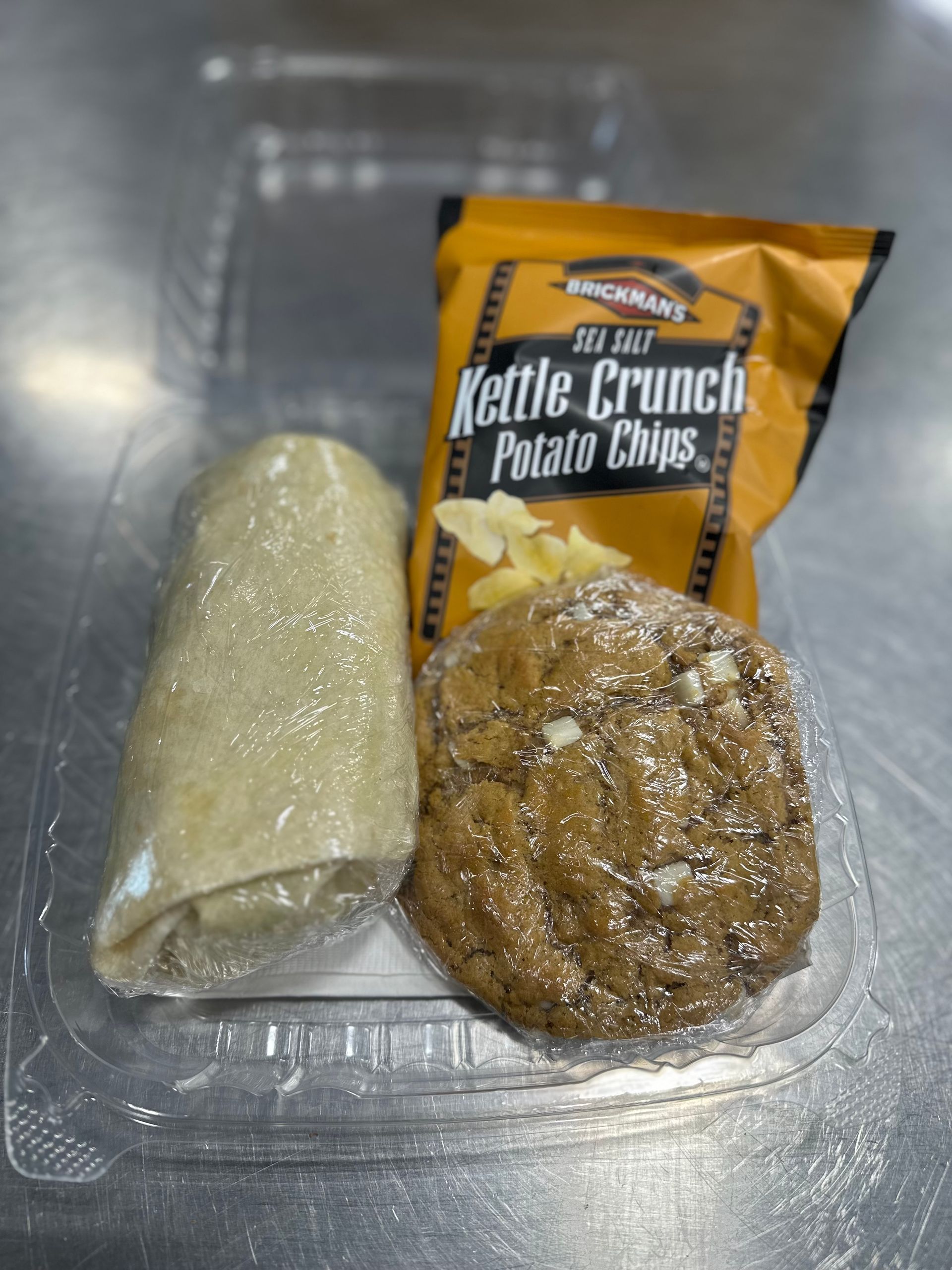 Lunch container with a wrapped item, cookie, and bag of chips.