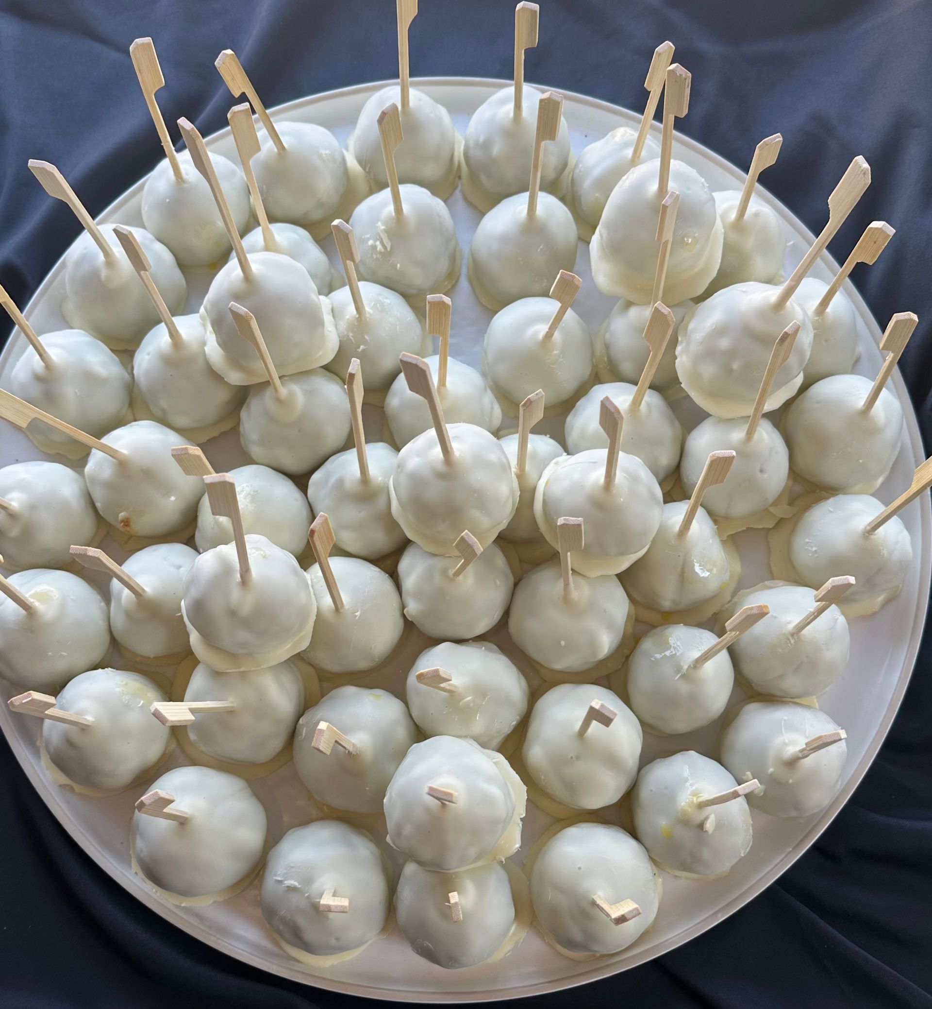 A circular plate filled with numerous white chocolate-covered cake pops, each on a small stick.