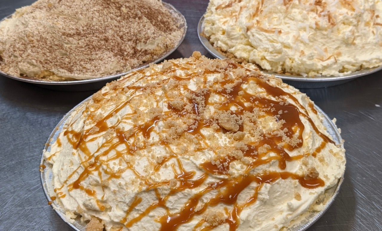 Three pies on a gray surface: one with cinnamon crumbs, one with toasted coconut, and one with caramel drizzle and crust.