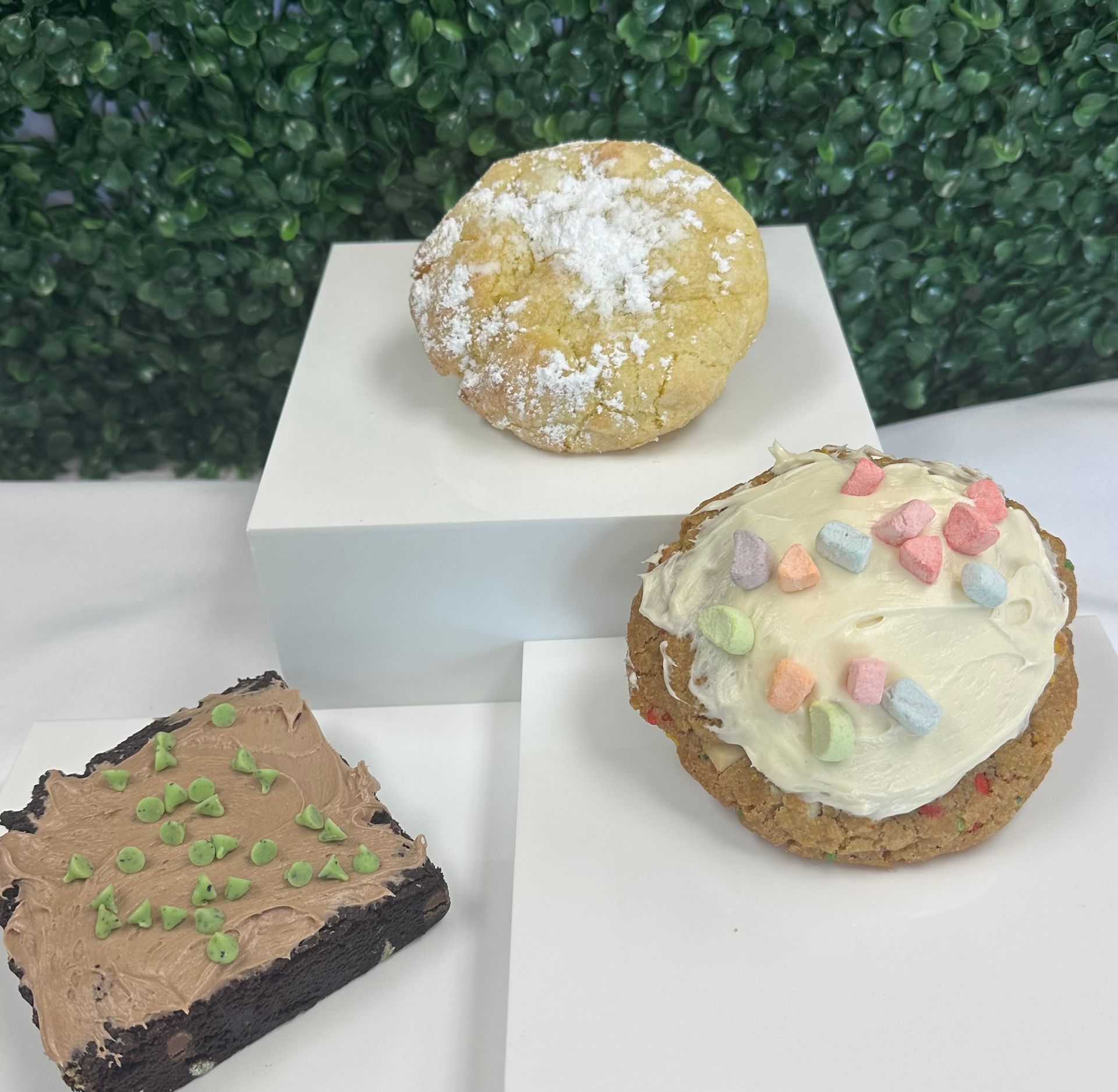 Three decorated pastries on white stands with green hedge backdrop