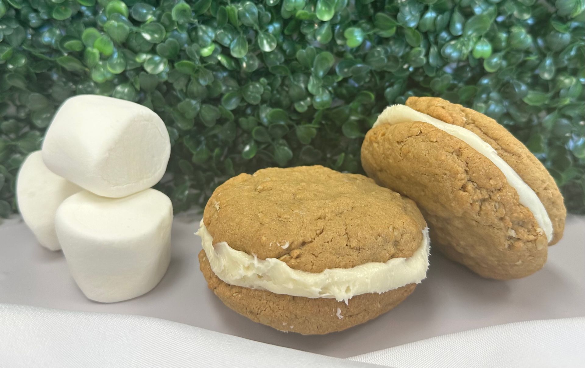 White marshmallows and two sandwich cookies with cream filling on a white surface, against a green background