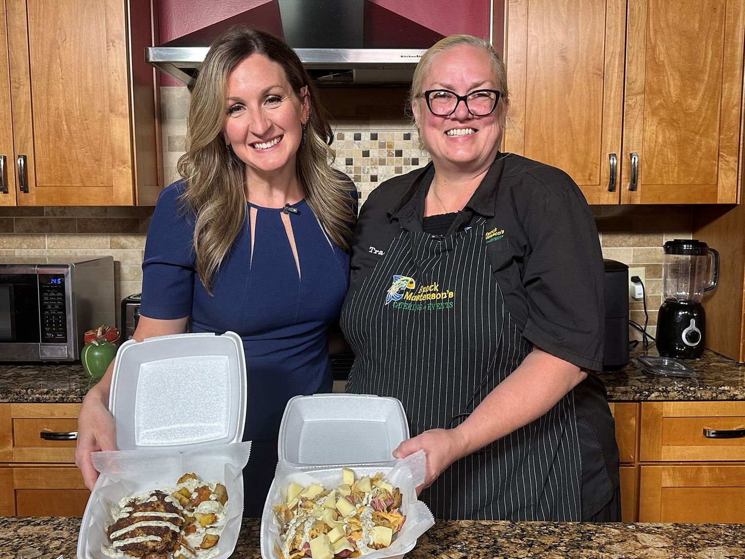 Two people in a kitchen holding open takeout containers with food.