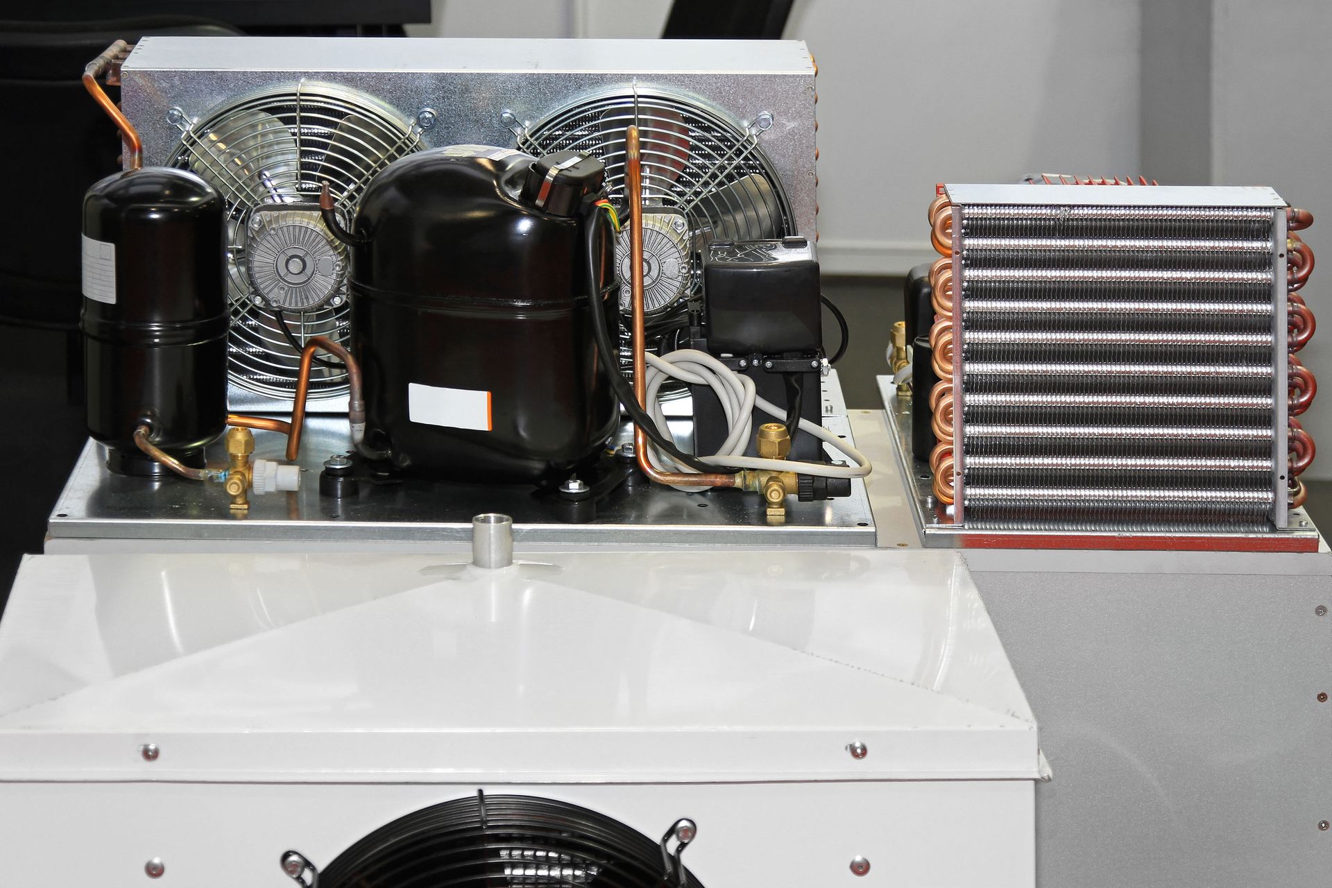 A refrigeration unit with compressor, condenser coil, and fan, mounted on a white box.