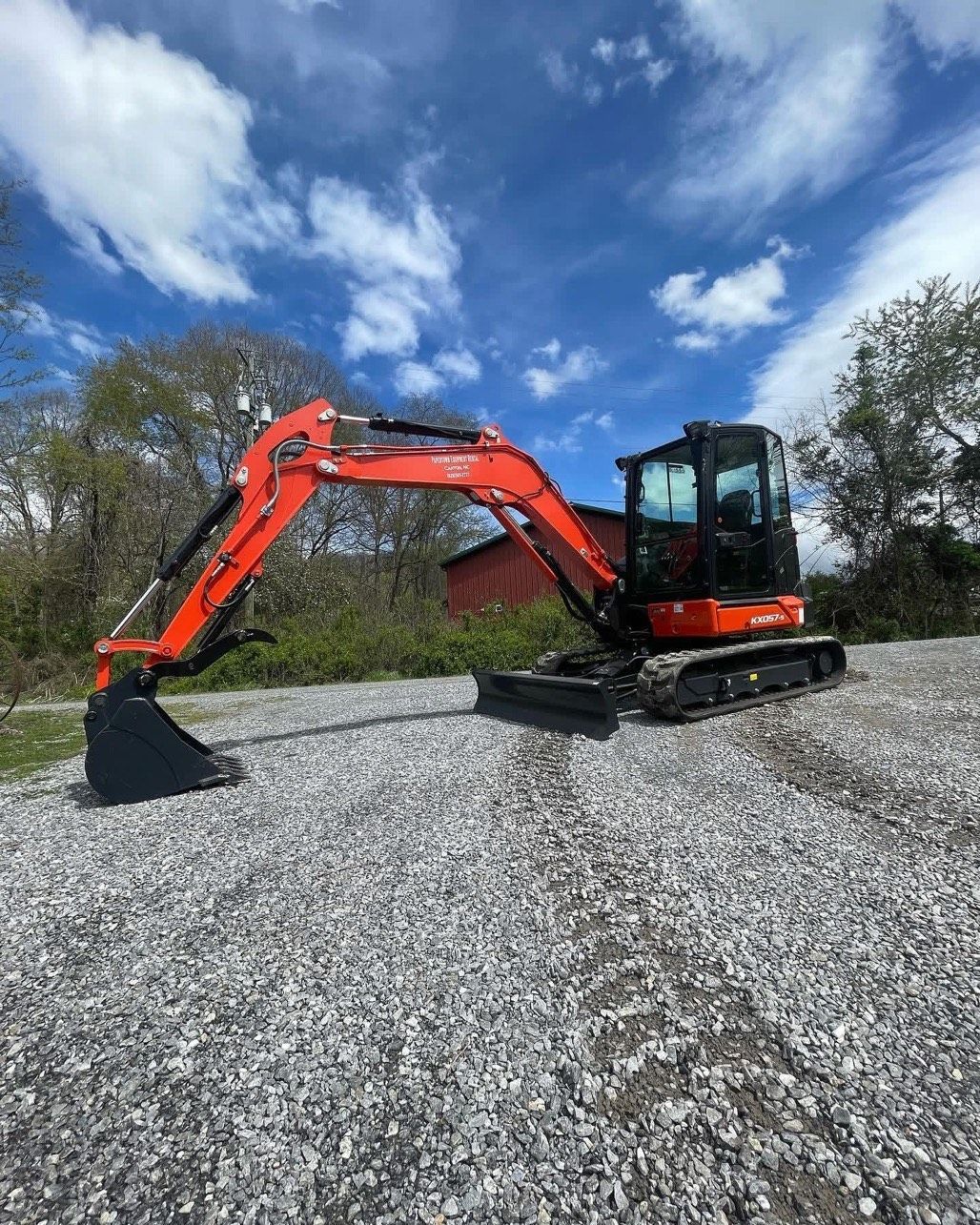 A red and black excavator is parked in front of a sign.