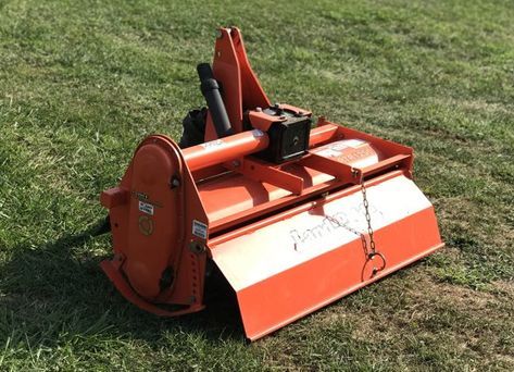 An orange and white machine is sitting on top of a lush green field.