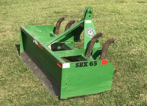 A green tractor blade is sitting on top of a lush green field.