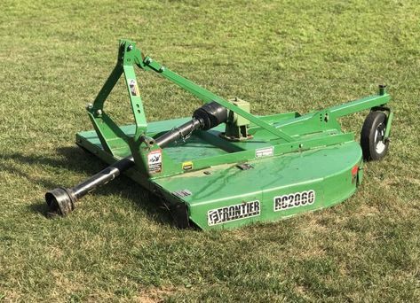 A green lawn mower is sitting on top of a lush green field.