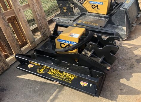 A construction machine is sitting on the ground next to a wooden fence.