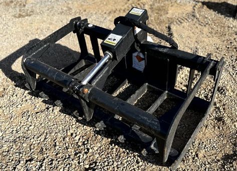 A black grapple bucket is sitting on top of a gravel road.