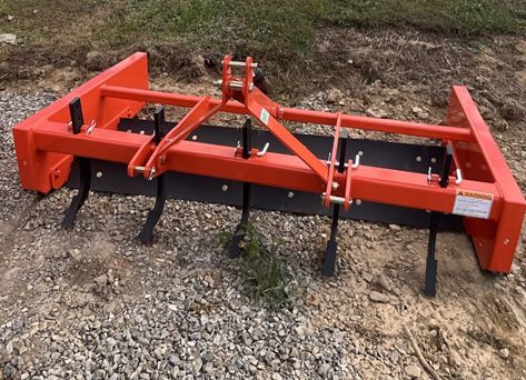 Orange box blade attachment for a tractor with ripper teeth.