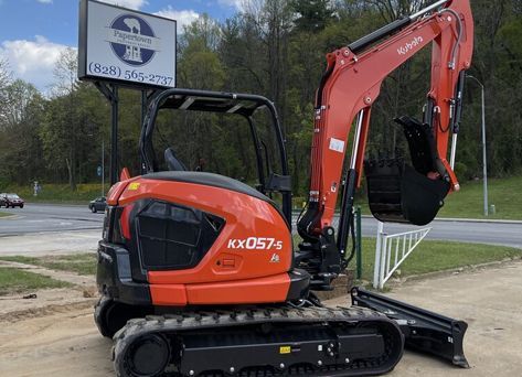 A red and black excavator is parked in front of a sign.