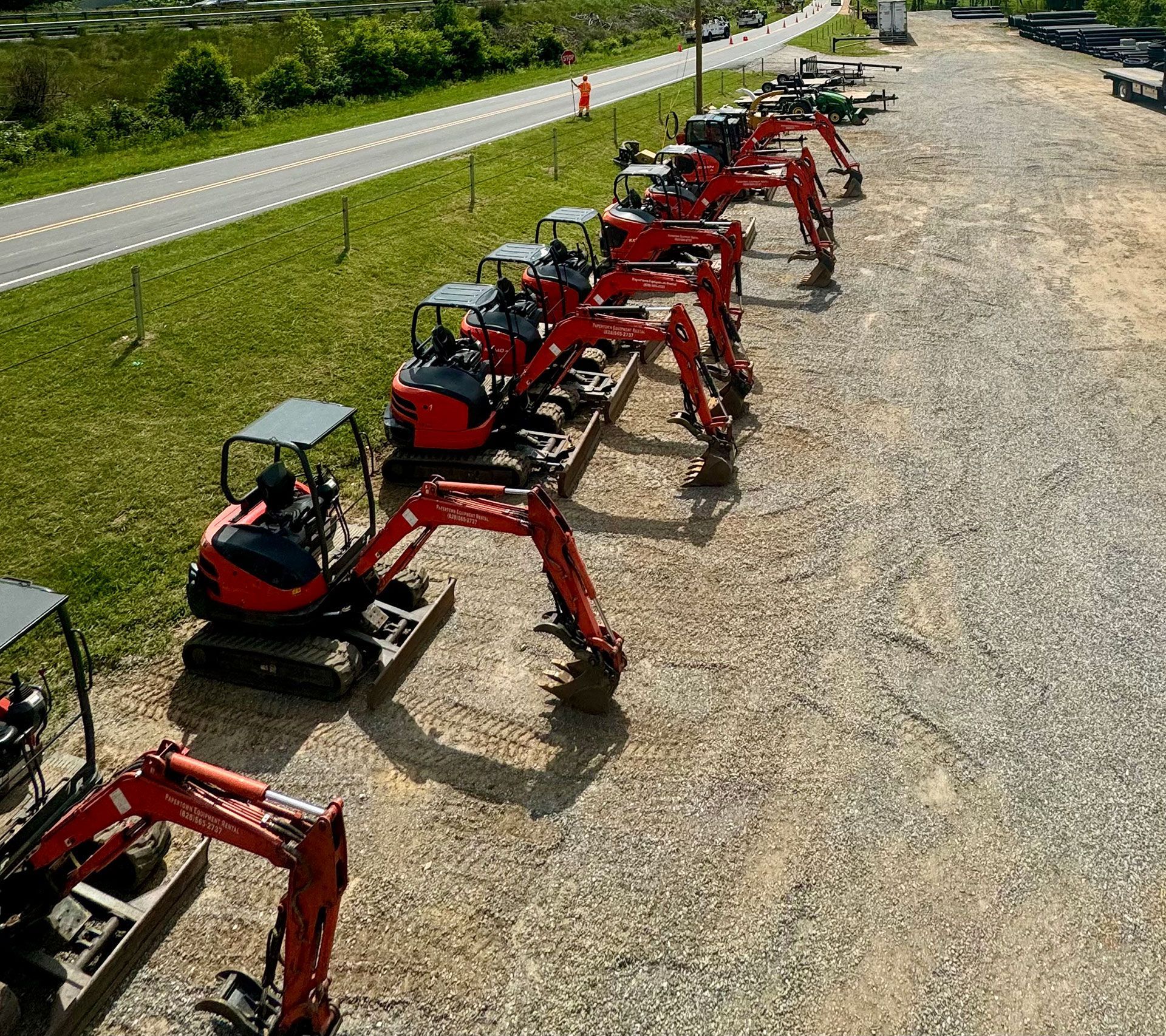 A row of red excavators are parked in a gravel lot
