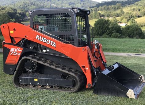 A red and black Kubota skid steer is parked in a grassy field.