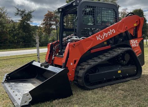 A red and black Kubota skid steer is parked in a grassy field.